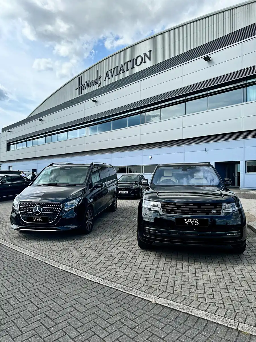Two luxury black chauffeur vehicles, a Mercedes-Benz van and a Range Rover SUV, parked in front of Harrods Aviation terminal.